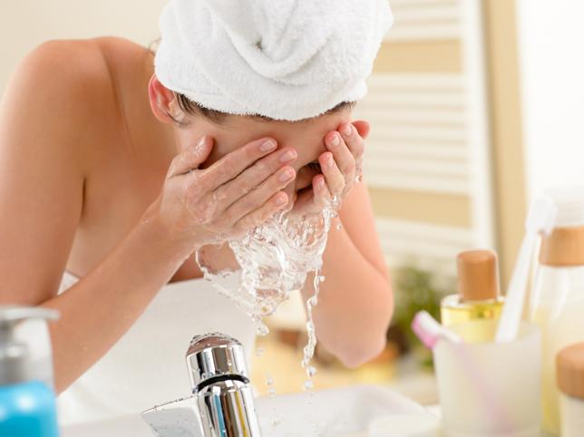 Mujer lavando su rostro despues de haber suado productos de belleza limpios