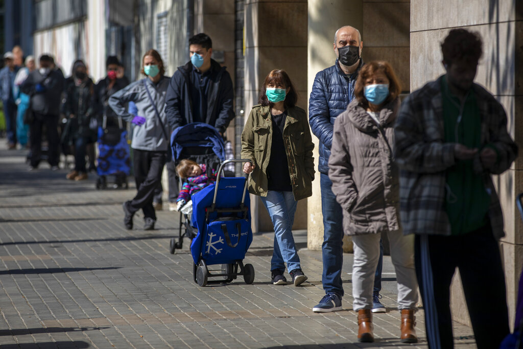  Personas con mascarillas se forman para comprar provisiones en una tienda durante el brote de coronavirus en Barcelona, España 