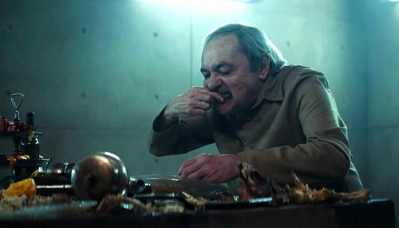 Filme el hoyo, anciano centado en la mesa comiendo con sus manos que están llenas de grasa al igual que su rostro